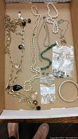 Jewelry assortment including pearl necklaces and bracelets, jade bracelet, gold chain necklace with mixed stone charms, a metal bangle, and small bags of earring parts shown in a box.