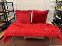 Two red velvet pillows and one red textured throw blanket displayed on chair