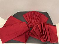 Large red folded tablecloth and ten folded red napkins laid out on a black surface, showing texture and color.