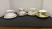 Four Royal Albert tea cup and saucer sets with different floral patterns and gold accents.