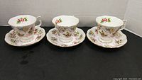 Three Royal Albert bone china cups with Canadian emblem and floral decoration alongside matching saucers, arranged on flat surface.