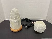 Selenite tower lamp and candle holder together on black surface with power cord coiled beside them.