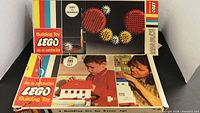 Photo of two vintage LEGO boxes, one Gear Set and one 285 piece Building Toy set with imagery of children playing.