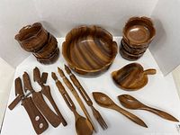 Large wooden salad bowl in center with six smaller wooden bowls arranged around it plus various wooden salad utensils and tongs