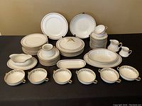 Full view of the 59-piece Limoges dinnerware set arranged on a black cloth showing plates, bowls, cups, pitchers, and serving dishes in cream with gold trim and floral decoration.