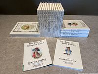 Photo of all 23 Beatrix Potter miniature books arranged in stacks by format showing front cover art of 'The Tale of Benjamin Bunny' and 'The Tale of Tom Kitten' softcover editions.