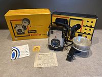 Full view of vintage Kodak Brownie Bull's-Eye Flash Camera with flash attachment, original yellow box, black inner box, and printed manuals displayed on table.