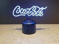 Coca Cola neon lamp turned on showing bright white neon logo on black base.