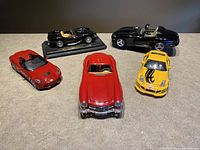 Five die cast model cars grouped together showing variety of models and colors including red, yellow, and black cars