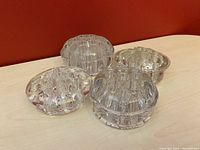 Four clear vintage glass flower frogs placed on a wooden surface, showing tops and sides.