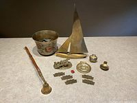 Mixed lot of brass collectables on flat surface showing all items including brass sail boat, bucket, pipe, plaques, and small items.