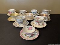 Photo showing all ten vintage tea cups and matching saucers arranged on a flat surface, displaying various floral and ornamental patterns from different brands.
