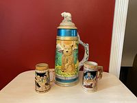 Full view of the three vintage beer steins including the large hand painted bear stein with lid and two smaller Trimont Ware steins