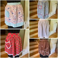 Five vintage handmade aprons displayed on a mannequin and table, showing various retro patterns and details