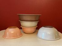 Five vintage Pyrex mixing bowls arranged showing upside down bowls in peach, cream, and brown tones.