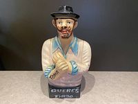 Front view of the handpainted ceramic figurine showing facial details, hat, hands with inscription, and base text