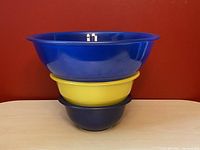 Three nested Pyrex mixing bowls in two shades of blue and one yellow, stacked inside each other, showing size difference.