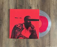 Vinyl record partially removed from bright red album jacket, clear translucent colored vinyl disk with orange label visible