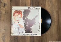 Photo of David Bowie Scary Monsters vinyl record partially out of illustrated jacket. Album art visible along with black vinyl showing original label.