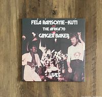 Front cover photo of album titled 'Fela Ransome-Kuti and The Africa '70 with Ginger Baker Live!'. Album cover and vinyl sealed in shrink wrap. Shows vintage style full-color live performance image.