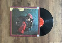 Photo showing album jacket with Janis Joplin image and red vinyl record partially removed from sleeve, placed on a wooden surface.