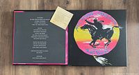 Photo of the closed front cover of the box set showing artwork of a cowboy riding a horse with colorful sunset background, also showing the inner liner and a small insert with text inside the box.