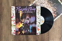 Photo of the Purple Rain LP vinyl record partially out of the album cover on a wooden surface. Covers the front of the jacket