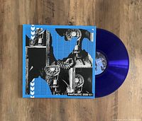 Blue translucent vinyl record partially out of its jacket on wooden surface. The jacket has black and white images of rotary telephones with blue text background.