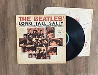 Photo shows The Beatles' Long Tall Sally vinyl record partially removed from original album jacket and white inner paper sleeve with red markings. The album jacket features a collage of band member photographs and title text.