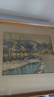 Framed winter landscape painting featuring river, trees, and hills in muted colors.