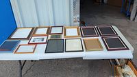 Fourteen assorted picture frames arranged on folding table, visible varying sizes, styles, wood and metal colors.
