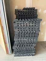 Stack of 2x2 ft black DBTile gym floor anti-slip tiles with quad blok edges shown stacked vertically.
