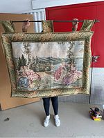 Front view of fine hanging tapestry showing countryside scene with three ladies under tree and lake background, bordered with leaf pattern.