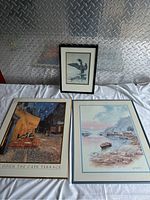 Three framed art prints shown together on white cloth background with silver diamond plate behind. Prints include Van Gogh Cafe Terrace, Carl Martin lakeside, and Loon Landing bird print.