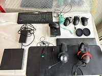 Wide view of gaming accessories displayed on white cloth including Alienware console, keyboard, mouse, large mousepad, two headsets, and three pairs of ear cushions.