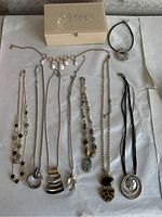 Overview of assorted costume jewelry necklaces arranged beside a beige jewelry box on a white surface.