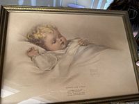 Framed sepia print of a sleeping child with title and signature on the bottom right corner.
