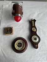 Overview of all items on white surface: brown outdoor lantern with red top, wooden wall-mounted barometer with thermometer and hygrometer, small square brass barometer.