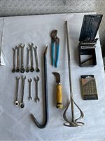 Photo showing combination wrenches, pliers, crowbar, drill bit set, curved yellow-handled tool, and mixing paddle