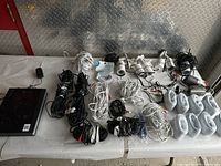 Overview of security equipment lot showing all cameras, DVR, bundled cables and ethernet cables spread on table.
