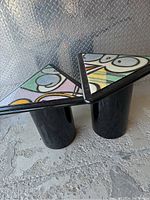 Front view of both triangular side tables side by side showing black lacquer finish and inset abstract tops
