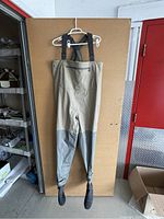 Full front view of Simms waders hung on hanger showing chest pocket and suspenders.