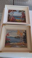 Both paintings stacked one on top of the other, showing vibrant landscape scenes and each framed in vintage painted wood frames.