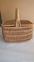 Front view of vintage rattan picnic basket with handle and hinged lid closed.