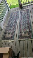 Two oriental style carpet runners laid flat on a wooden porch floor, showing general wear and need for cleaning