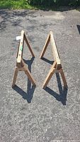 Two used wooden saw horses arranged on pavement, captured from above to show top surfaces and frames.