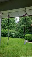 Two metal wind chimes hanging from porch eaves, visible against a backyard background with grass and trees.