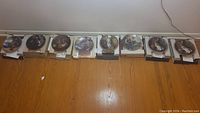 Eight Norman Rockwell limited edition collectible china plates displayed in their boxes on a hardwood floor.