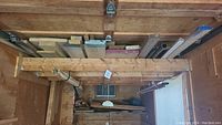 Assorted wood pieces stored on a high shelf in a wooden shed or garage, showing various sizes of boards, planks, and strips.