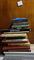 Stack of 14 oversized books against wood background showing titles like Desert Images, Canada by David Craig, An J Casson, The Age of Napoleon, Blake's Dante, World Atlas.